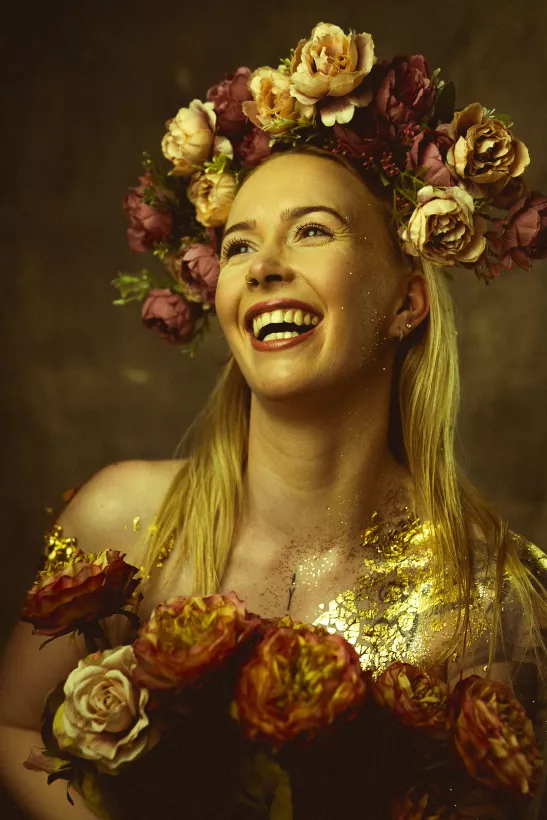 Lachende Frau mit prachtvollem Blumenkranz aus Rosen und Goldakzenten auf der Haut