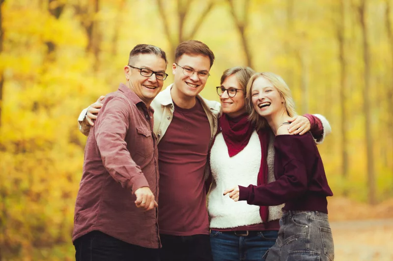 Lachendes Familienportrait von vier Personen im herbstlichen Wald.