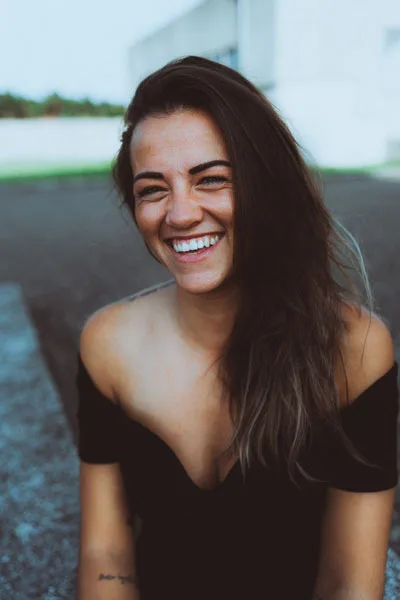 Lachendes Porträt einer Frau mit langen dunklen Haaren und schwarzem Off-Shoulder-Oberteil.