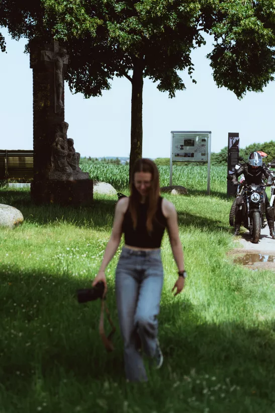 Lifestyle-Fotografie einer Frau beim Spaziergang durch eine sommerliche Parklandschaft mit historischem Steinkreuz