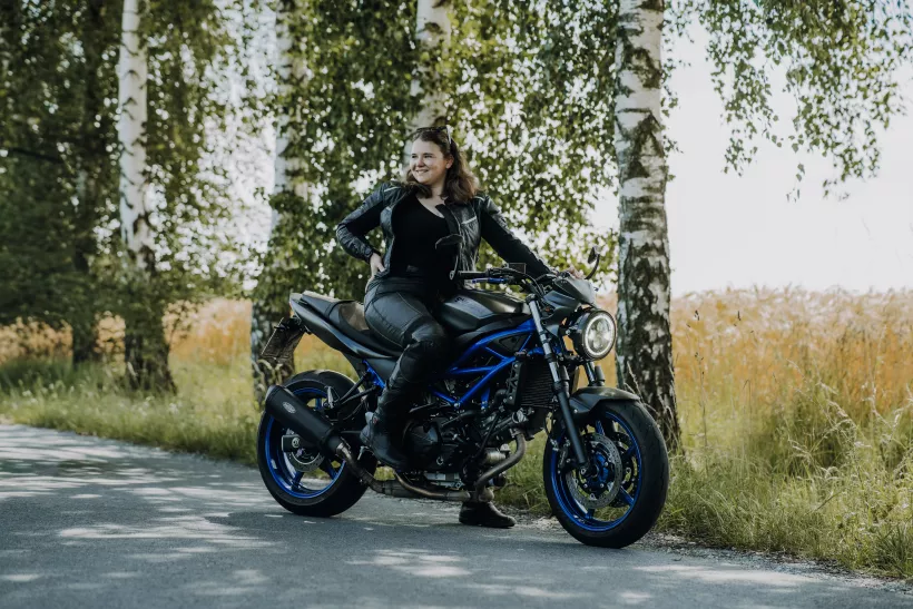 Outdoor-Portrait einer lächelnden Frau in schwarzer Lederkleidung auf einem blauen Motorrad