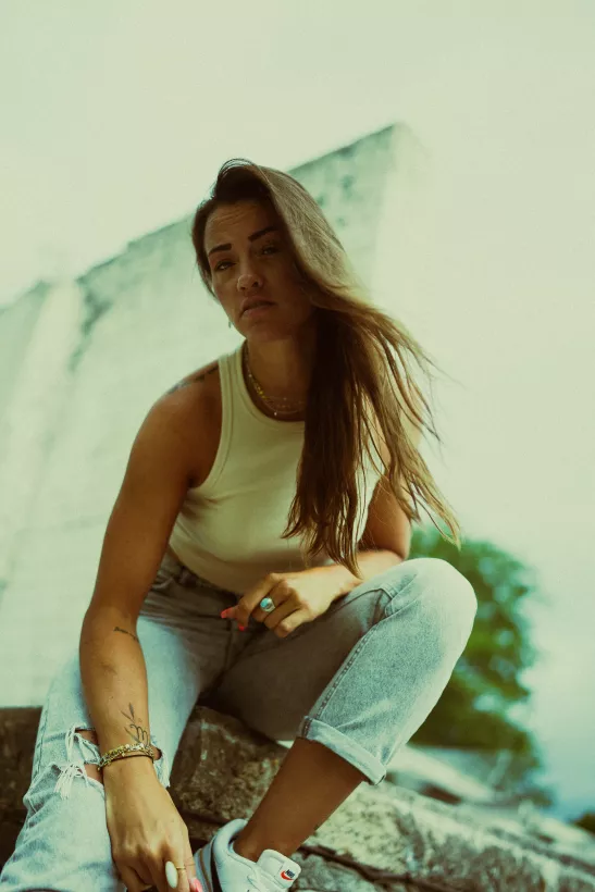 Lifestyle-Portrait einer Frau in weißem Top und Jeans vor einer hellen Betonwand