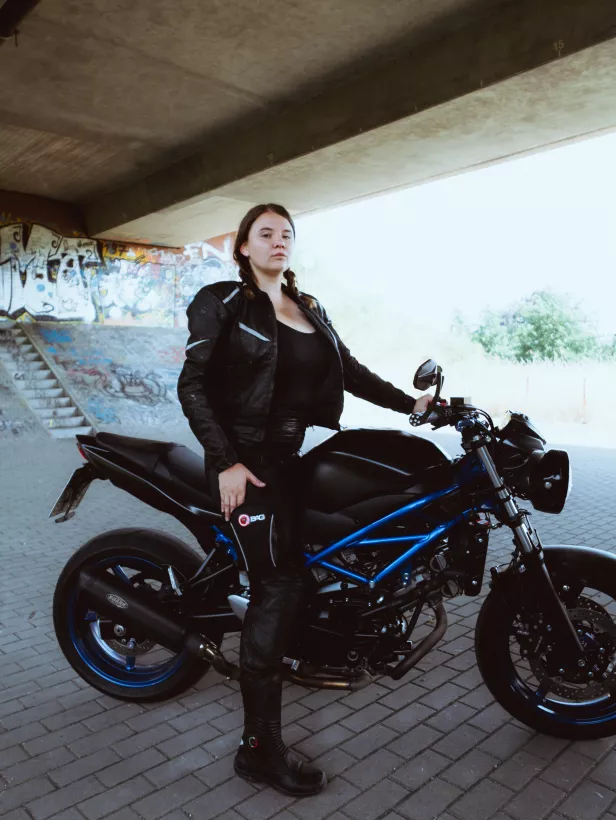 Urbanes Lifestyle-Portrait einer Frau in schwarzer Lederkleidung neben einem Motorrad vor einer Graffiti-Wand