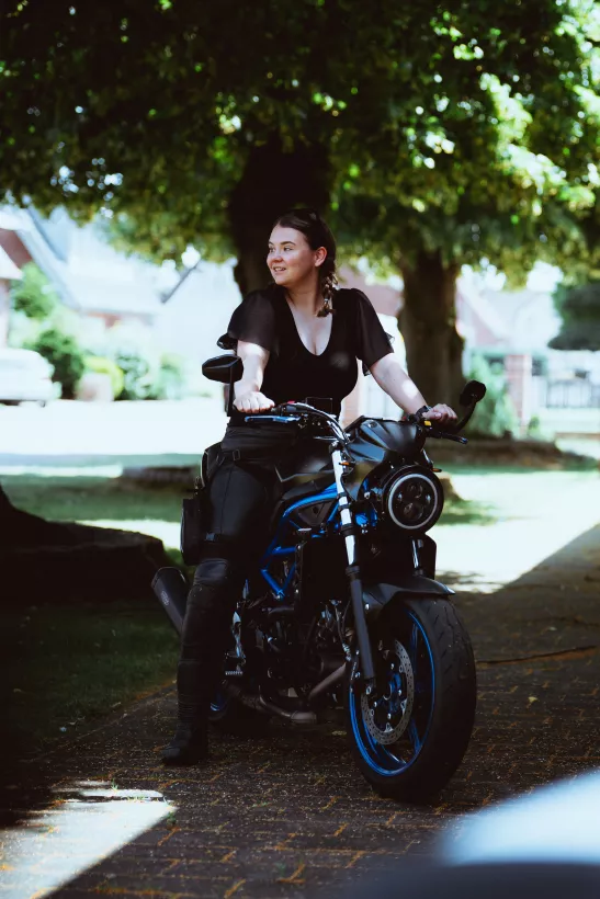 Lifestyle-Portrait einer lächelnden Frau auf einem schwarzen Motorrad im Grünen
