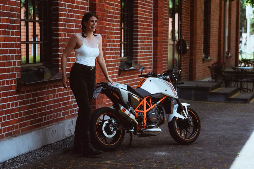 Lifestyle-Portrait einer lächelnden Frau neben einem weißen Motorrad vor einer