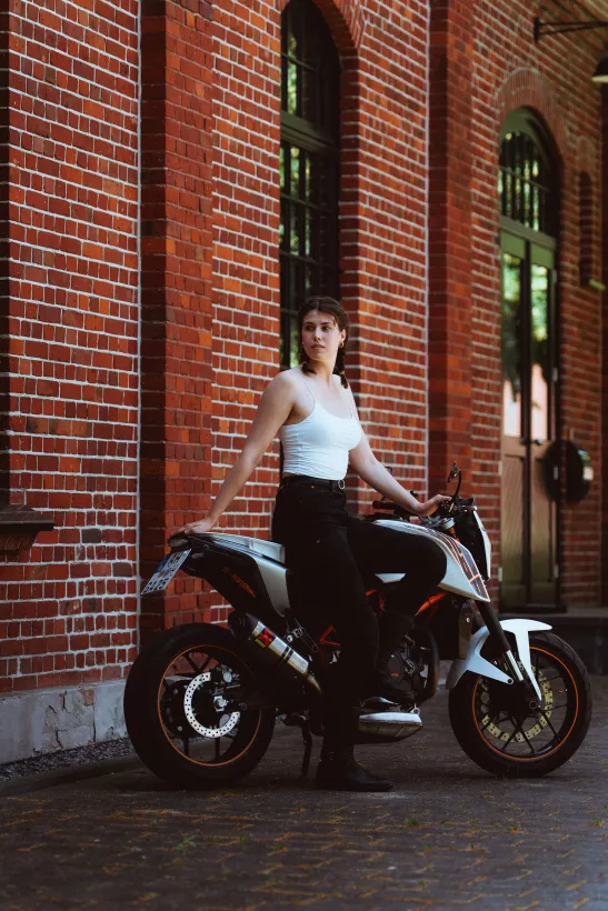 Lifestyle-Portrait einer jungen Frau auf einem weißen Motorrad vor einer roten Backsteinwand