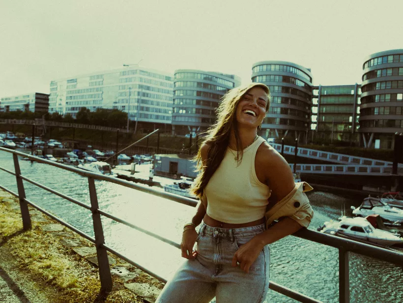 Fröhliches Lifestyle-Portrait einer lachenden Frau vor moderner Architektur am Wasser