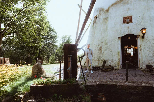 Ein Mann in heller Kleidung steht vor einer alten weißen Windmühle.