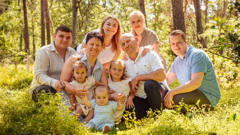 Mehrgenerationen-Familienfoto in einer sonnendurchfluteten Waldlandschaft.