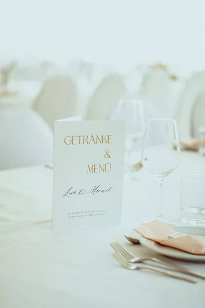 Menükarte für Getränke und Speisen auf einer hellen, festlich gedeckten Hochzeitstafel.