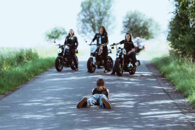Lifestyle-Fotografie einer am Boden liegenden Person und herannahenden Motorradfahrern auf einer Landstraße