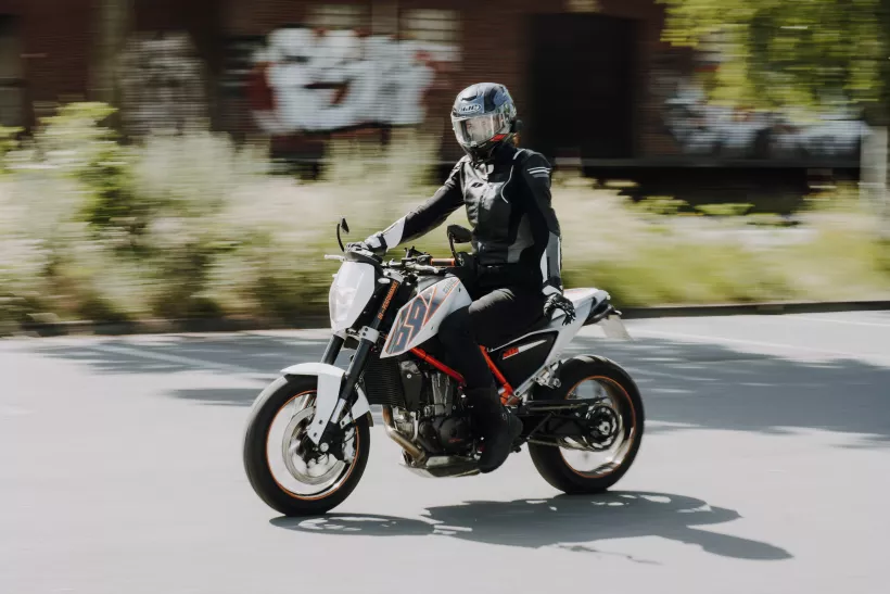 Dynamisches Actionfoto eines Motorradfahrers in schwarzer Schutzkleidung auf einer asphaltierten Straße.