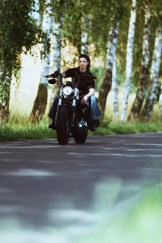 Outdoor-Aufnahme einer Frau auf einem schwarzen Motorrad in einem Birkenwald