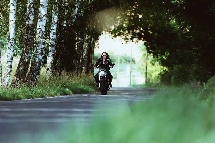 Outdoor-Aufnahme einer Motorradfahrerin auf einer von Birken gesäumten Straße