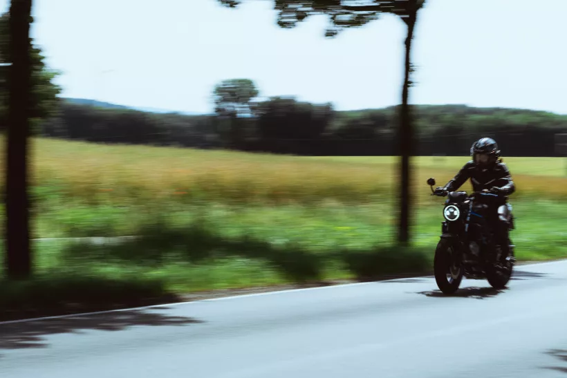 Dynamisches Actionfoto eines Motorradfahrers auf einer Landstraße durch eine grüne Landschaft.