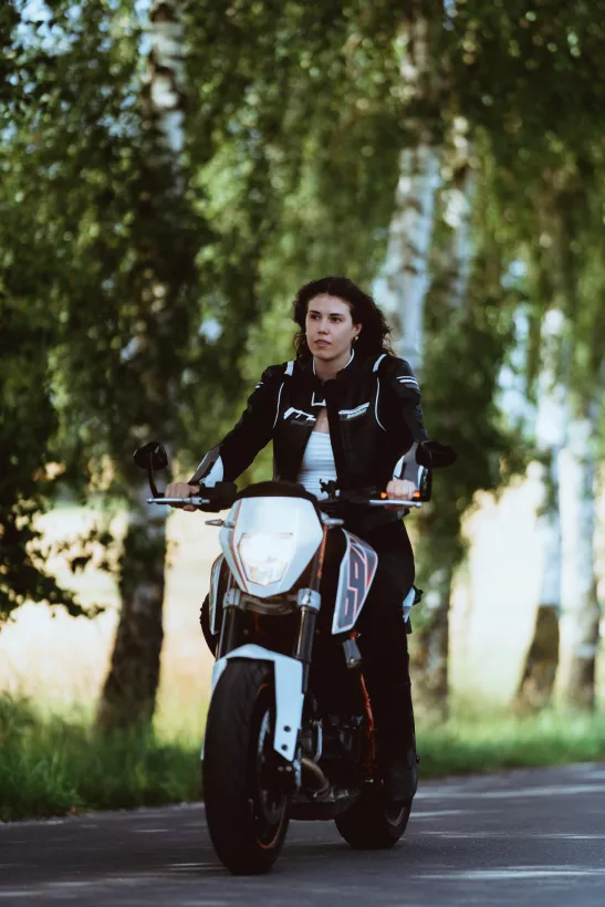 Outdoor-Portrait einer Frau auf einem weißen Motorrad in einem Birkenwald