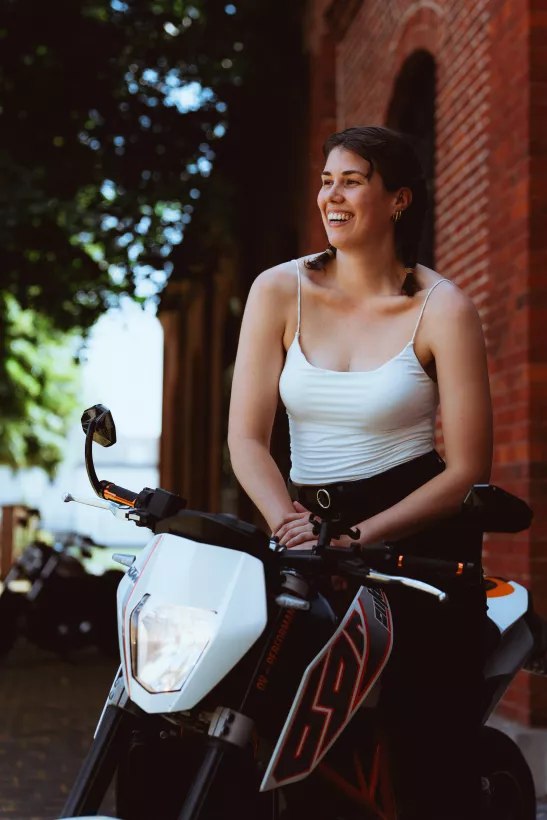 Lachendes Outdoor-Portrait einer Frau auf einem Motorrad vor einer