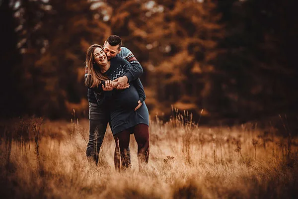 Liebevolles Paarshooting einer schwangeren Frau und ihres Partners in einer herbstlichen Landschaft.