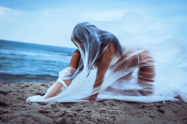 Person am Strand unter wehendem, weißem, transparentem Stoff.