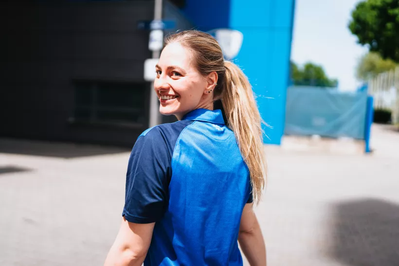 Portrait einer lächelnden Frau mit blondem Pferdeschwanz in einem blauen Poloshirt