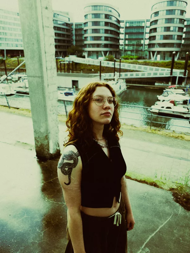 Portrait einer Frau mit Brille und Schlangentattoo vor moderner Architektur am Wasser