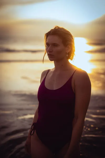 Portrait einer Frau in einem dunkelvioletten Badeanzug am Strand bei Sonnenuntergang