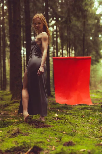 Portrait einer Frau in einem dunklen Kleid vor einem leuchtend roten Stoff im Wald.