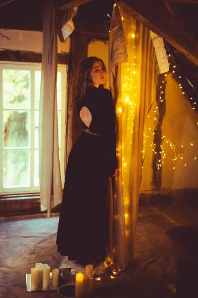 Portrait einer Frau in einem dunklen Kleid zwischen herabhängenden Stoffbahnen und warmen Lichterketten.