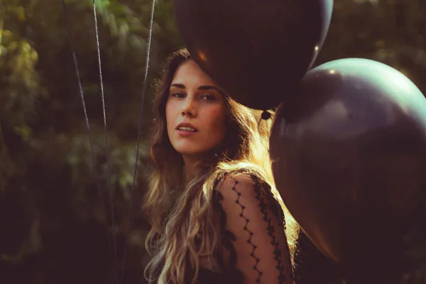 Portrait einer Frau mit langem blondem Haar zwischen dunklen Ballons.
