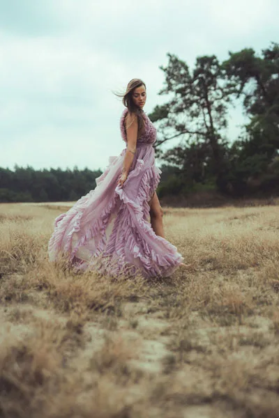 Portrait einer Frau in einem fließenden, lila Rüschenkleid auf einer Wiese vor Waldkulisse
