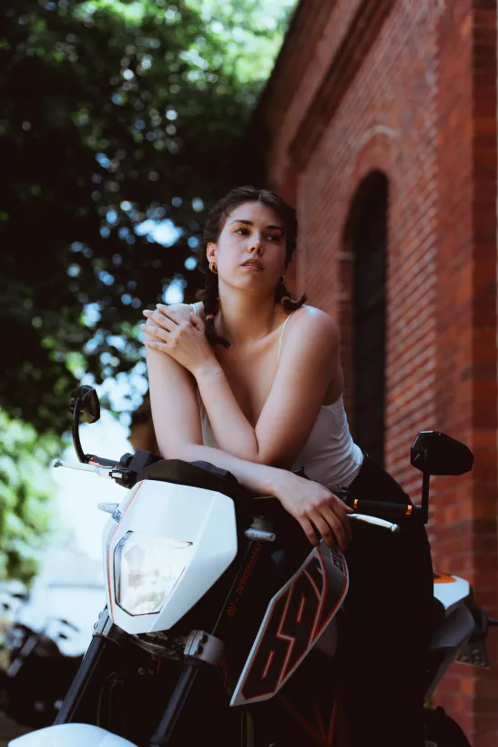 Portrait einer jungen Frau, die auf einem weißen Motorrad vor einer roten Backstein