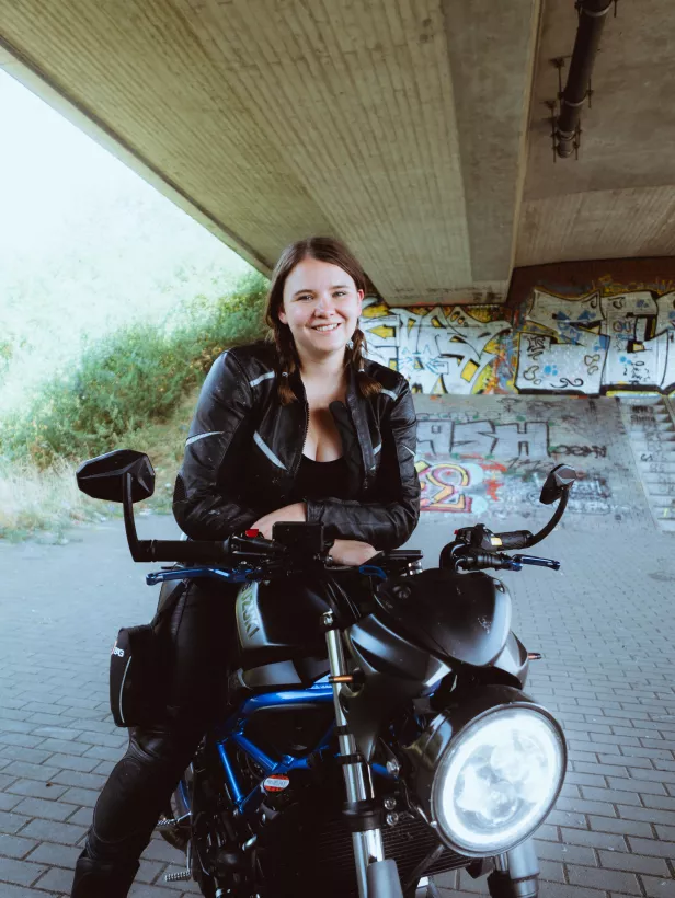 Portrait einer lächelnden Frau auf einem Motorrad vor einer Graffiti-Wand im Unterpass