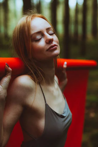 Portrait einer Frau mit rötlichem Haar und geschlossenen Augen in einem Wald.