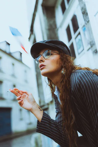 Portrait einer Frau mit Schiebermütze, Sonnenbrille und Nadelstreifen-Sakko