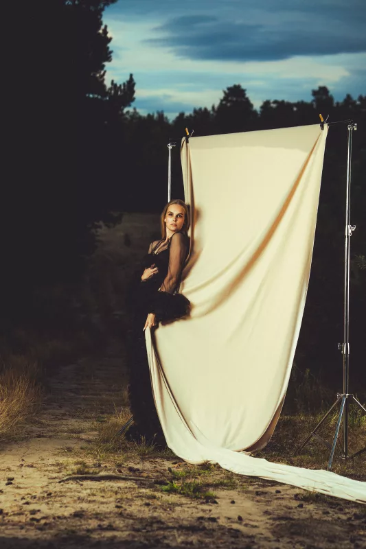 Portrait einer Frau in schwarzem Kleid hinter einem cremefarbenen Stoffhintergrund im Wald