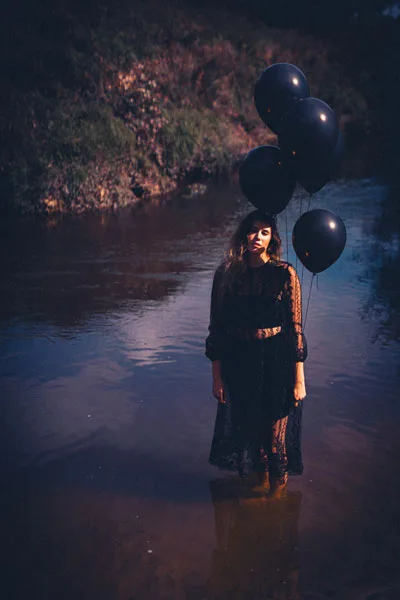 Portrait einer Frau mit schwarzen Ballons im flachen Wasser.