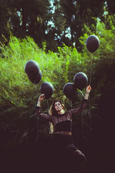 Portrait einer Frau mit schwarzen Luftballons vor grünem Laub.