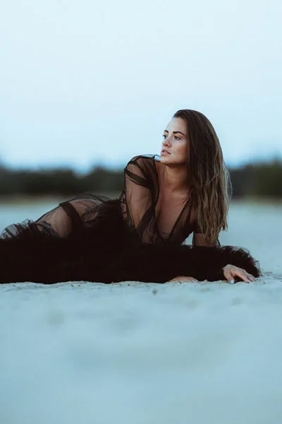 Portrait einer Frau in einem schwarzen, transparenten Kleid am Strand bei Dämmerung.