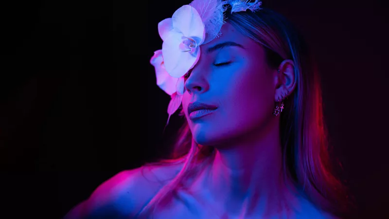 Portrait einer Frau mit weißen Orchideen im Haar unter blauem und rosa Licht.