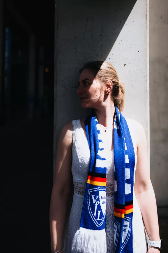 Portrait einer Frau im weißen Spitzenkleid mit blauem Schal vor einer Betonwand bei starkem Sonnenlicht