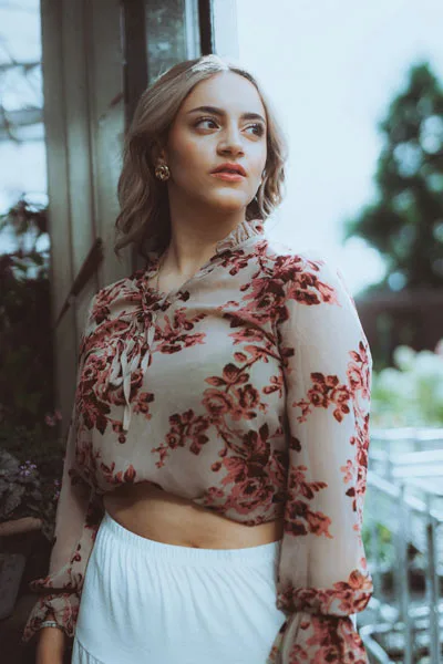 Portrait einer jungen Frau mit blonden Haaren in einer floral gemusterten Bluse.