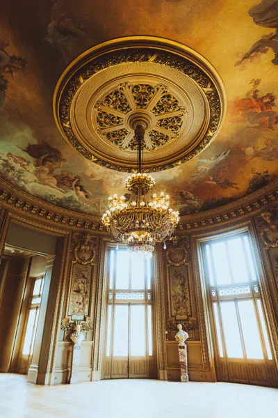 Prachtvoller Saal mit einem großen Kristallkronleuchter unter einem kunstvollen Deckenfresko.