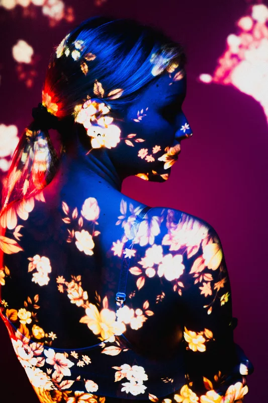 Profilporträt einer Frau mit floralen Lichtprojektionen auf Gesicht und Körper