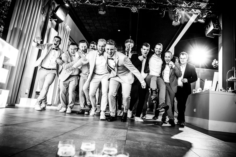 Schwarz-weiß Eventfoto einer lachenden Gruppe von Männern in festlicher Kleidung.