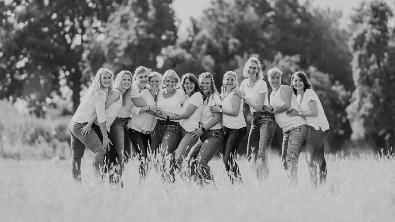 Schwarz-weiß Gruppenportrait lachender junger Frauen auf einer Wiese.
