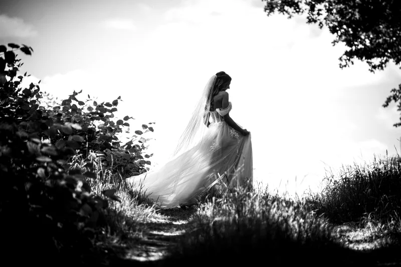 Schwarz-weiß Hochzeitsfoto einer Braut im hellen Kleid zwischen Bäumen und Sträuchern.