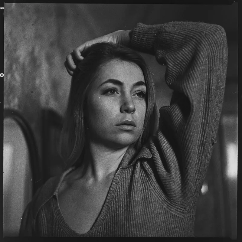 Schwarz-weiß Portrait einer Frau mit der Hand im Haar und einem Rippstrickpullover.