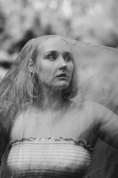 Schwarz-weiß Portrait einer Frau hinter einem feinen, transparenten Schleier.