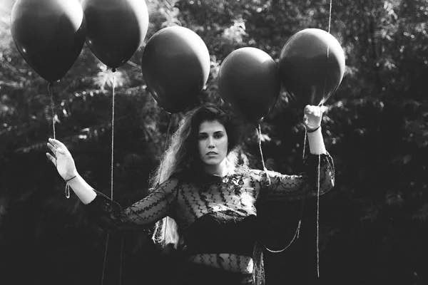 Schwarz-weiß-Portrait einer Frau mit langen Haaren, die mehrere dunkle Luftballons hält.