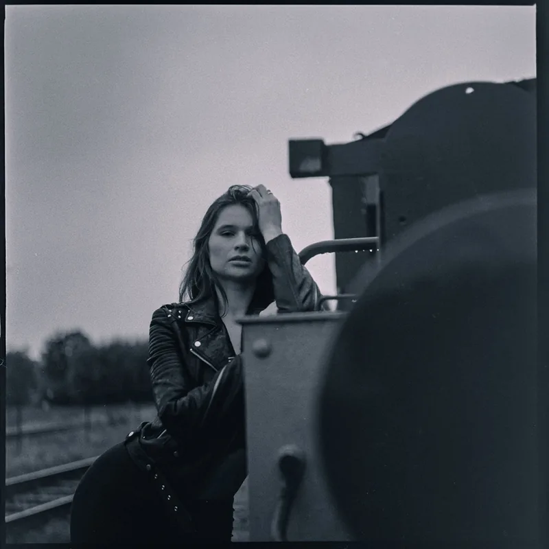 Schwarz-weiß Portrait einer Frau in Lederjacke, die an einem Waggon lehnt.